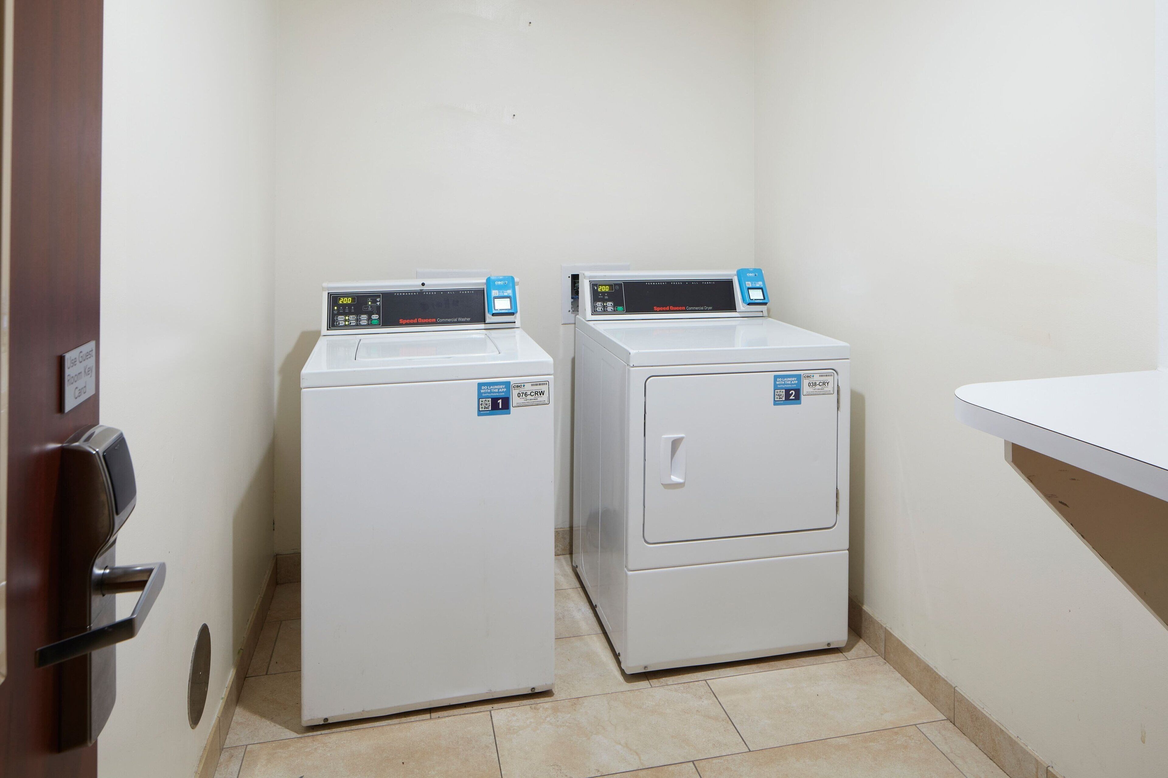 Two front-loading washing machines in a laundry room with a white sink and a door to the left.