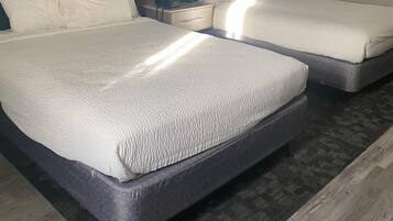 Ein Doppelbett mit strukturierter weißer Matratze und einem dunklen Kopfteil. Ein Nachttisch mit Lampe und Telefon ist vorhanden. Der Raum verfügt über eine blaue Akzentwand und eine Holzvertäfelung über dem Bett.