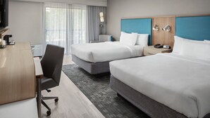 Una habitación de hotel con dos camas, un escritorio, una silla, un televisor y una ventana con cortinas.
