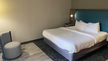 Una habitación de hotel con cama, una silla, una mesita de noche y una lámpara fijada a la pared.
