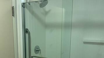Cabina de ducha con cerramiento de vidrio, un cabezal de ducha manual, un perchero y una puerta de vidrio.