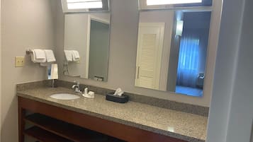 Un baño de hotel con encimera de granito, dos lavamanos, un espejo y un perchero para toallas.