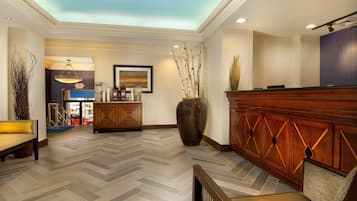 A hotel lobby with a herringbone floor pattern, a reception desk, a large vase, and a painting on the wall.