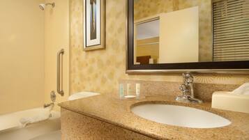 A bathroom with a granite countertop sink, a mirror, a towel rack, and a shower area.