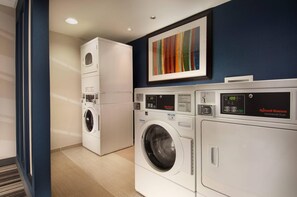 A laundry room with a front-loading washer and dryer, a stacked washer, and a colorful abstract painting on the wall. - Comfort Inn Downtown DC/Convention Center (Washington)