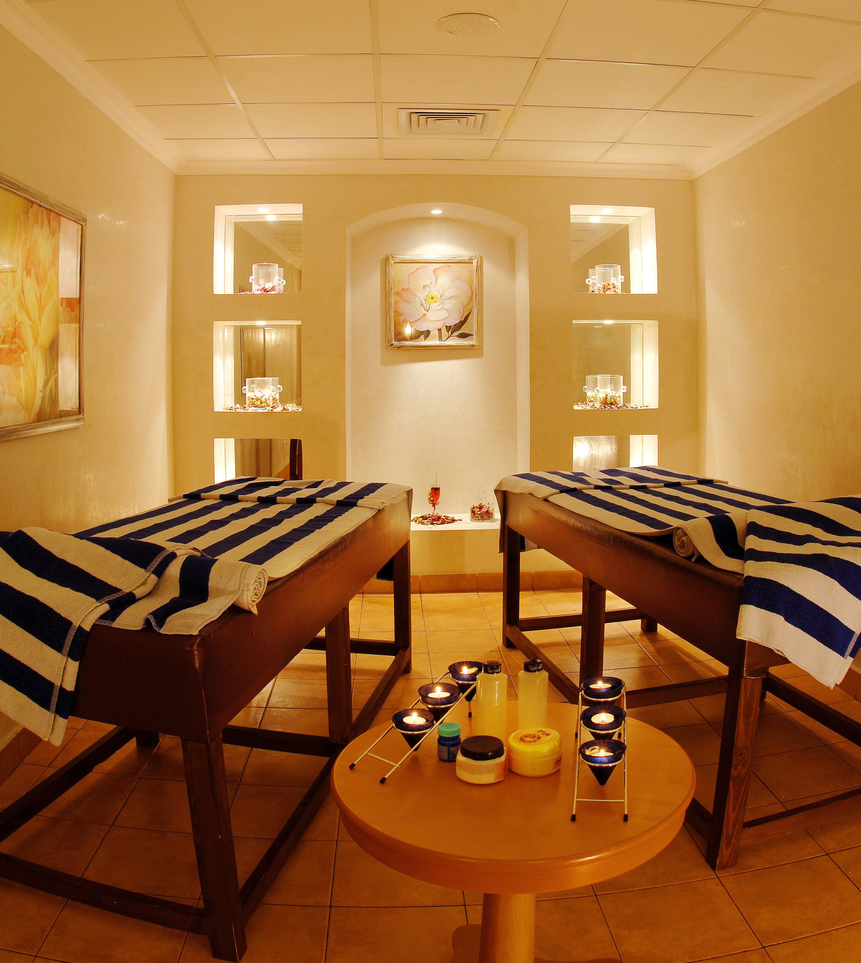 Ein Raum mit zwei Massagetischen, einem kleinen Tisch mit Kerzen und einem Gemälde an der Wand.