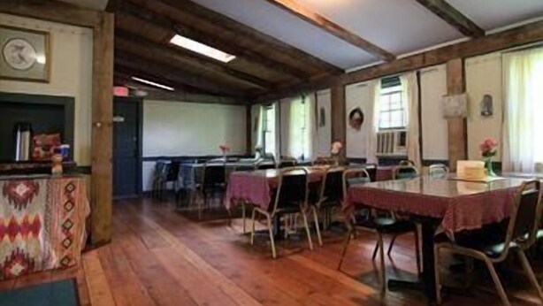 A dining area with wooden floors, tables with red tablecloths, and chairs. - Ladd Brook Inn (Pownal)