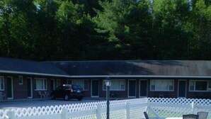 A poolside area with white lounge chairs and a table, surrounded by a white lattice fence. - Ladd Brook Inn (Pownal)