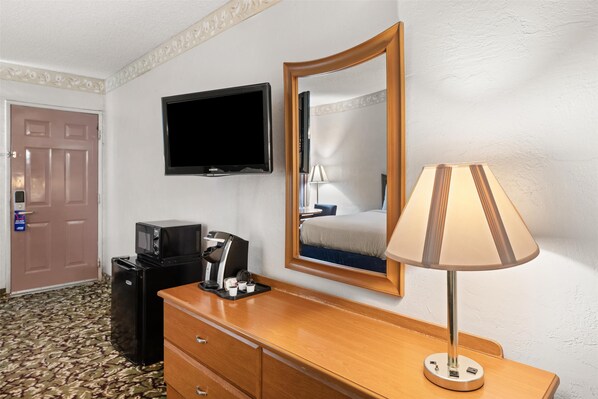 A hotel room with a wooden dresser, a television mounted on the wall, a mirror, a lamp, a microwave, and a refrigerator. - AMERICAS BEST VALUE INN BY SONESTA PECOS (Pecos)
