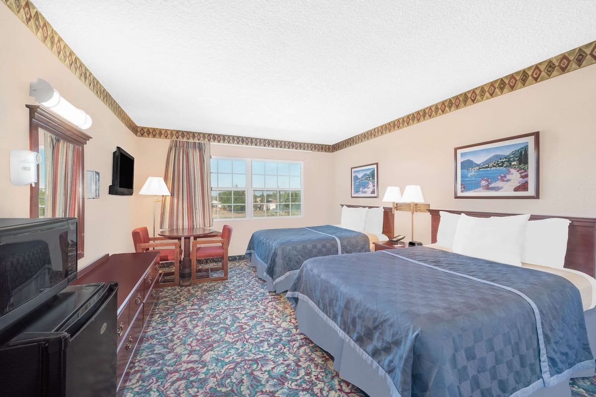 Une chambre d’hôtel avec deux lits, un bureau avec une chaise, une télévision et une fenêtre avec des rideaux.