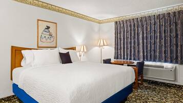 Une chambre d’hôtel avec un grand lit, un bureau, une chaise, une lampe et une fenêtre avec des rideaux.