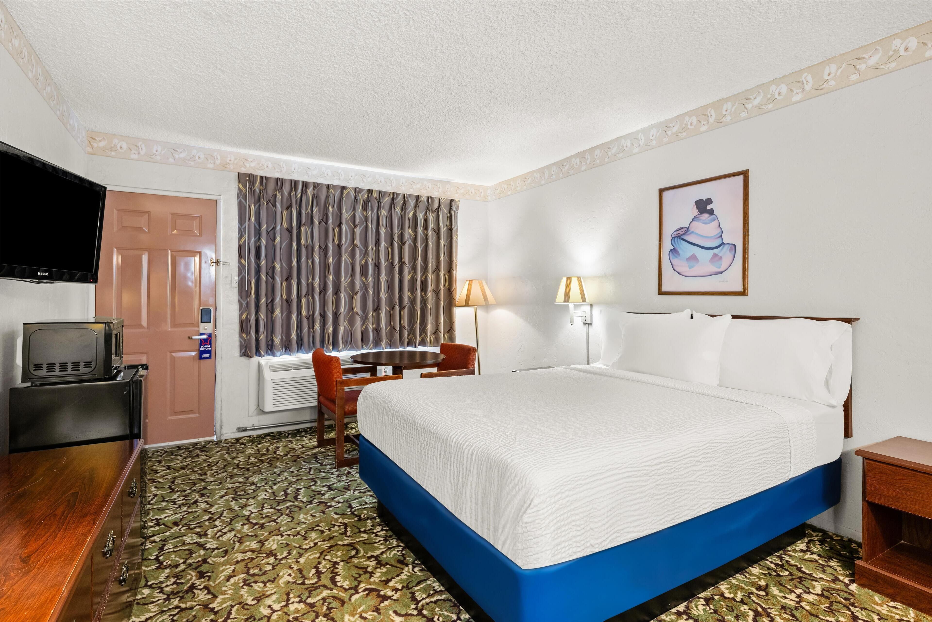 Una habitación de hotel con una cama, un escritorio, un televisor y una ventana con cortinas.