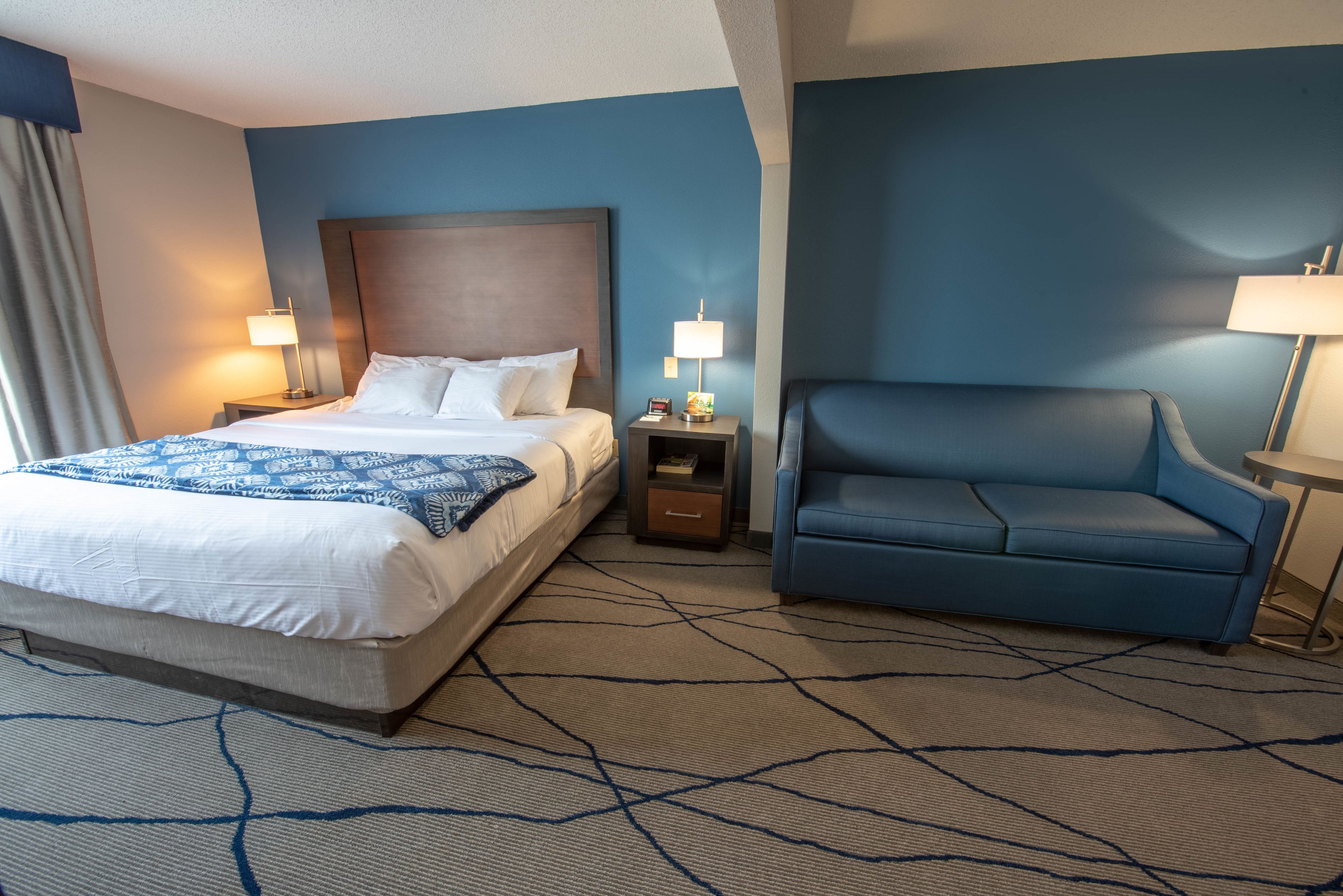 Une chambre d’hôtel avec un lit, un canapé bleu et deux tables de chevet avec des lampes.