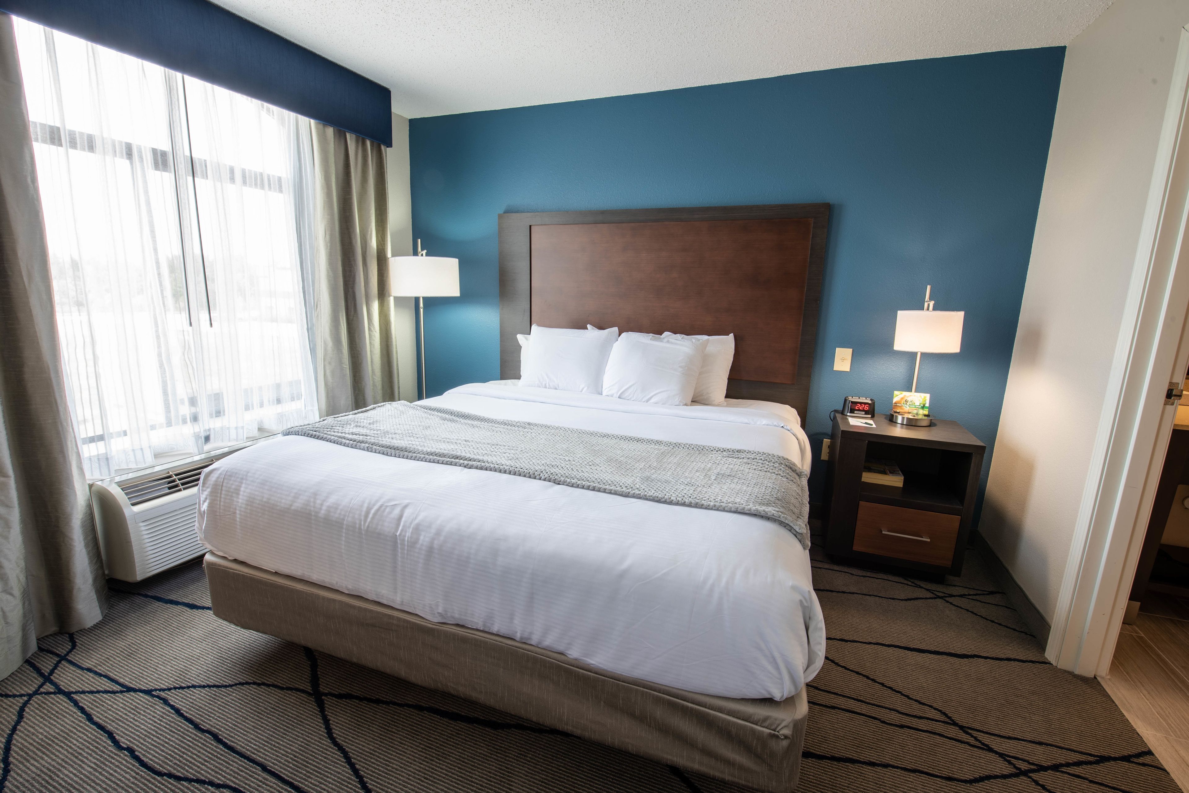 Una habitación de hotel con una cama grande, una mesita de noche con lámpara y una ventana con cortinas.