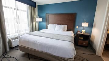 Una habitación de hotel con una cama grande, una mesita de noche con lámpara y una ventana con cortinas.