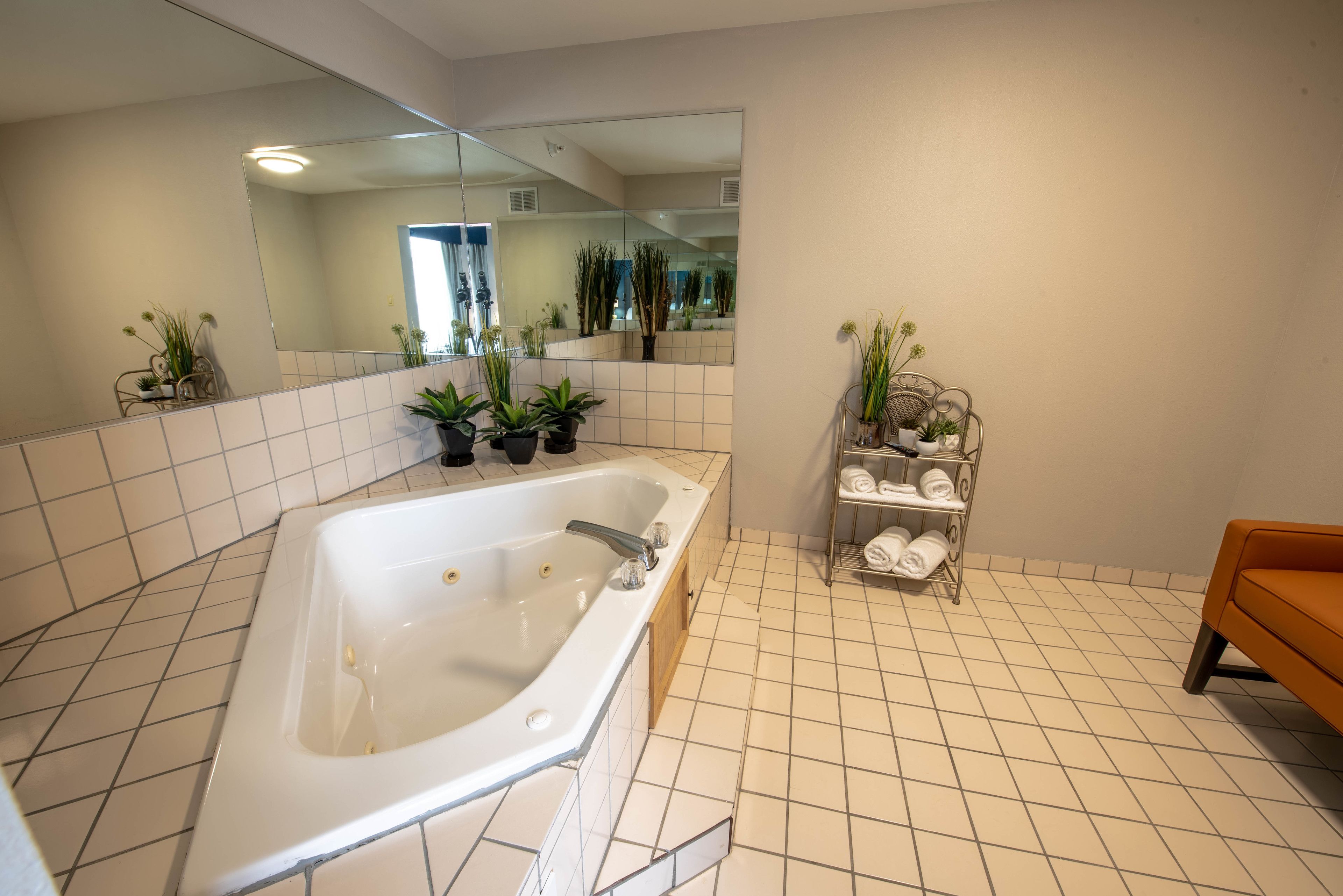 A modern bathroom with a large bathtub, tiled floor, a mirror, and potted plants.