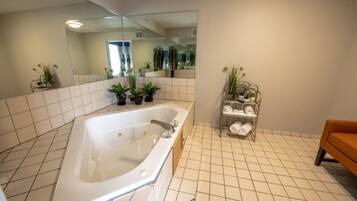 A modern bathroom with a large bathtub, tiled floor, a mirror, and potted plants.