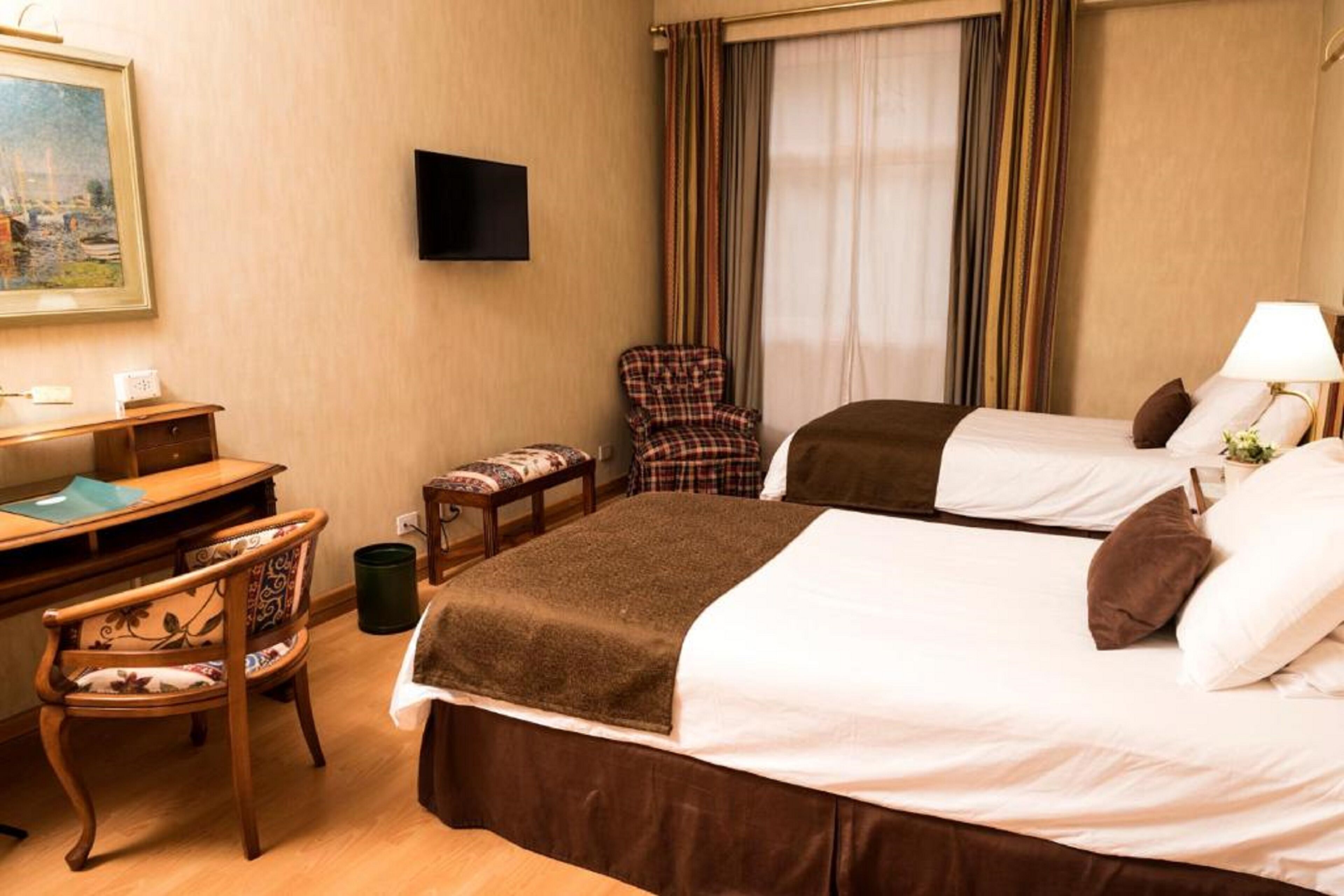 A hotel room with two beds, a desk, a chair, a TV, and a window with curtains.