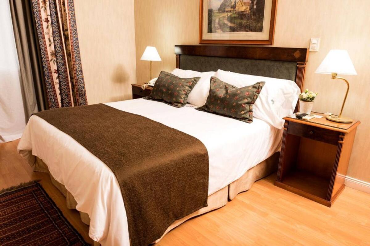 A neatly made bed with a brown blanket, two bedside lamps, and a framed picture on the wall.