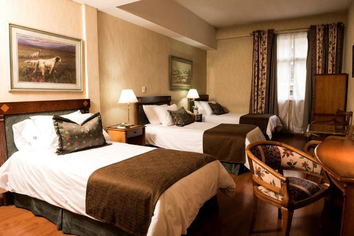 A hotel room with two beds, a wooden chair, a desk, and a painting on the wall.