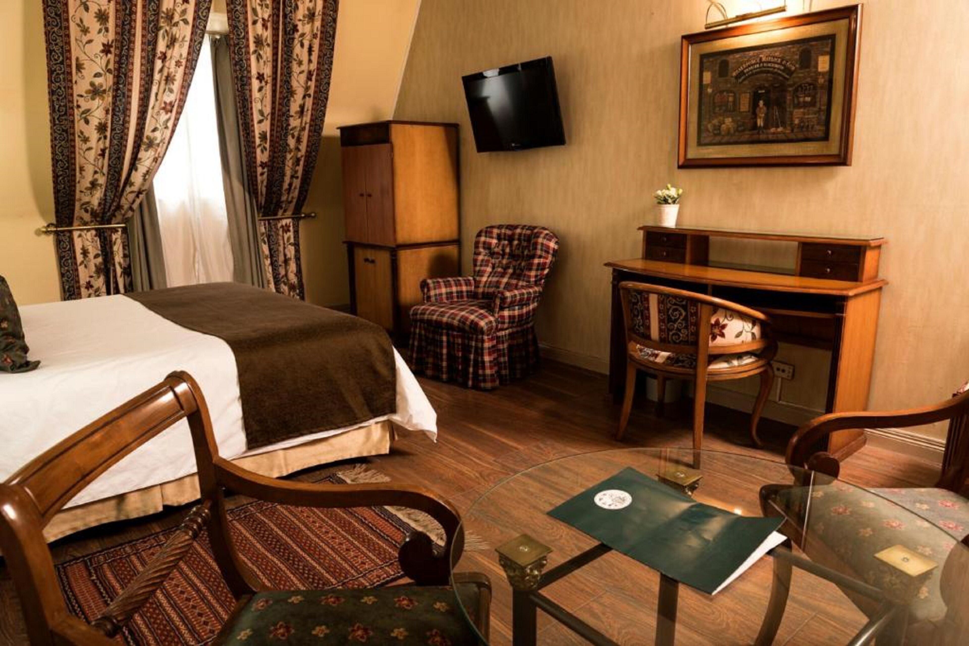Una habitación de hotel con cama, escritorio, silla, televisor y un cuadro en la pared.