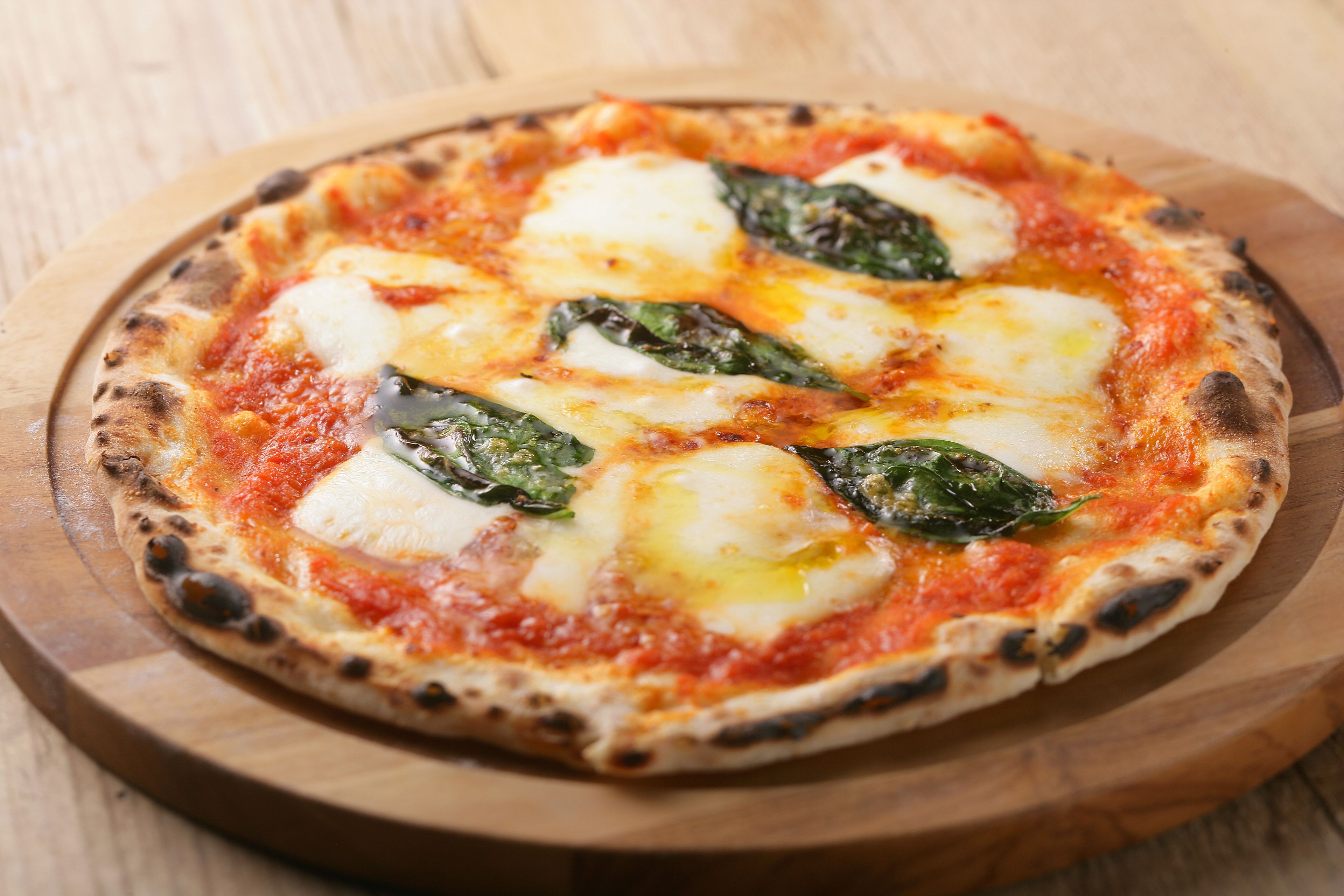 Una pizza con queso y espinacas sobre una tabla de madera.