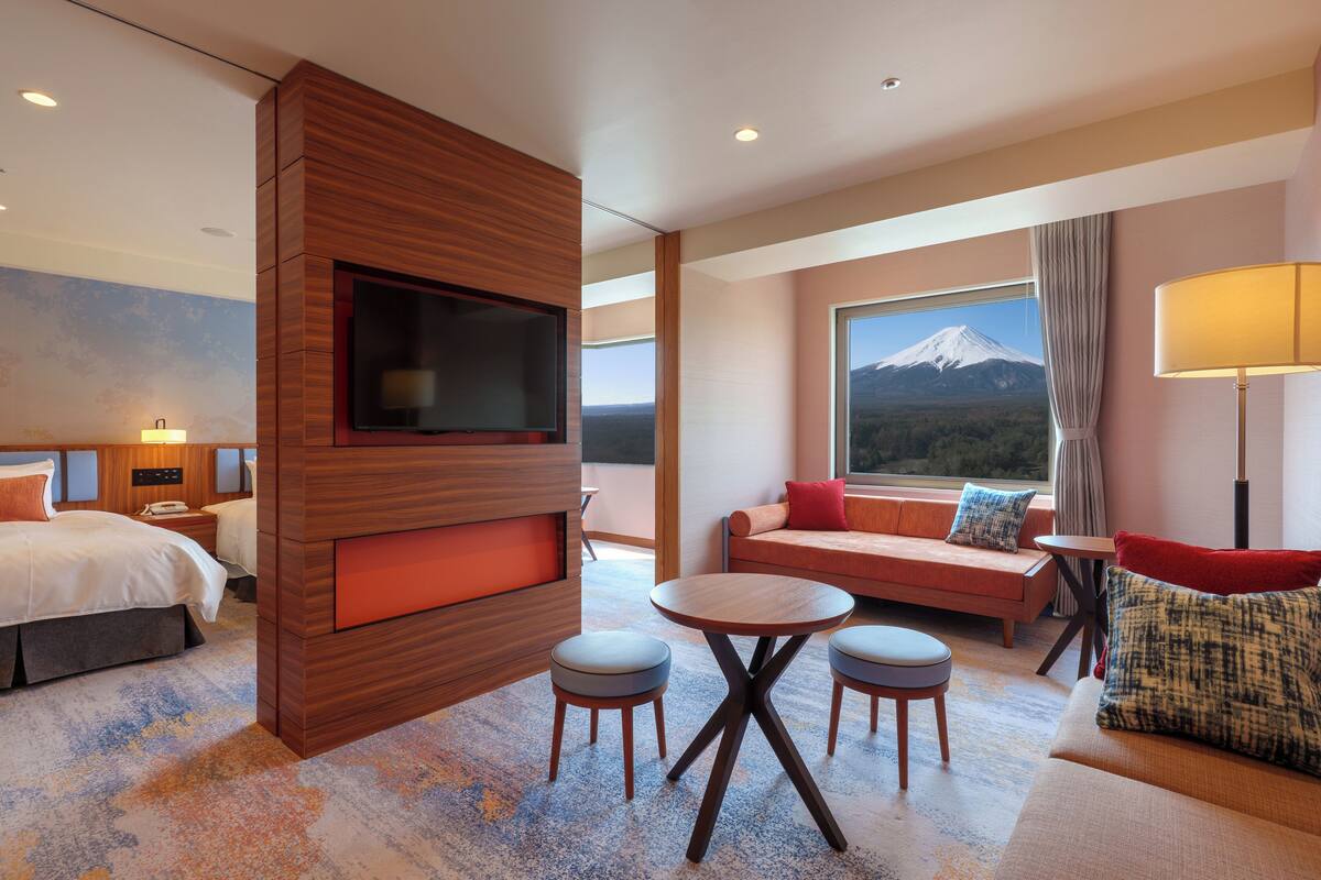 A hotel room with a bed, a TV, a sofa, a table, and a view of a mountain.