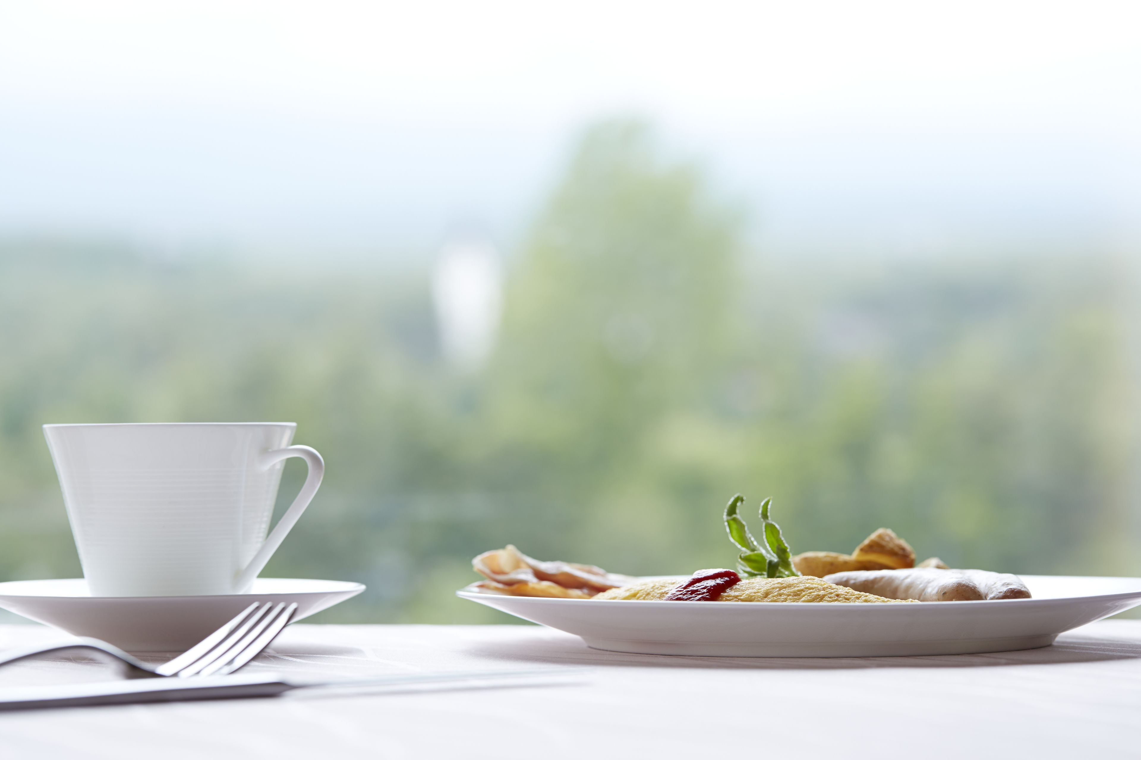 A white cup and saucer on a table with a plate of food and a fork.