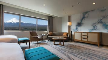 A hotel room with a large bed, a sofa, a chair, a small table, and a cabinet. There is a window with a view of a mountain.