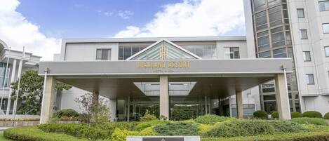 A modern hotel entrance with a covered walkway, a signboard, and well-maintained landscaping.