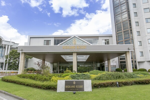 A modern hotel entrance with a covered walkway, a signboard, and well-maintained landscaping. - Highland Resort Hotel & Spa (Fujiyoshida)