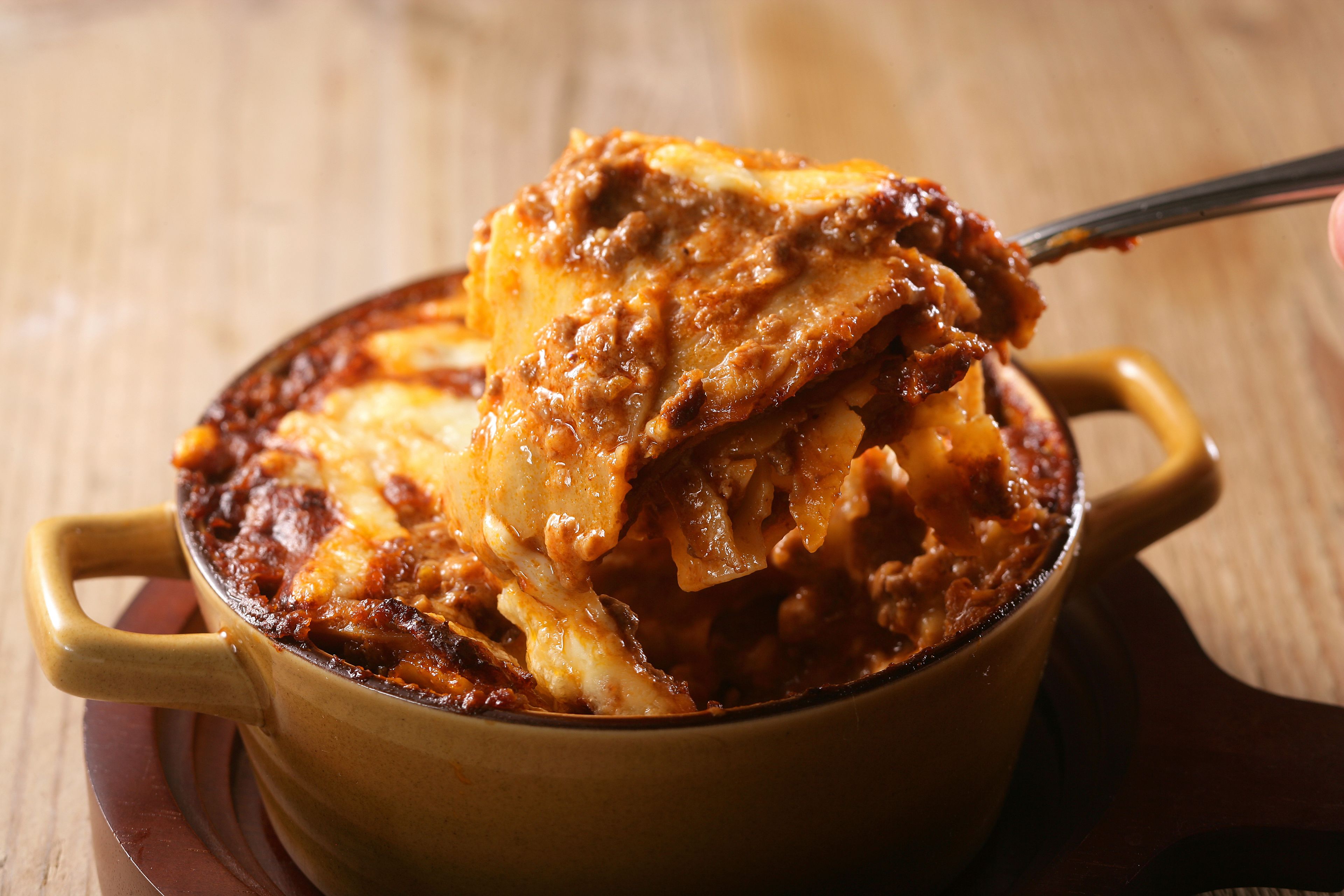 A close-up of a baked dish with a golden-brown crust, possibly lasagna, being lifted with tongs.