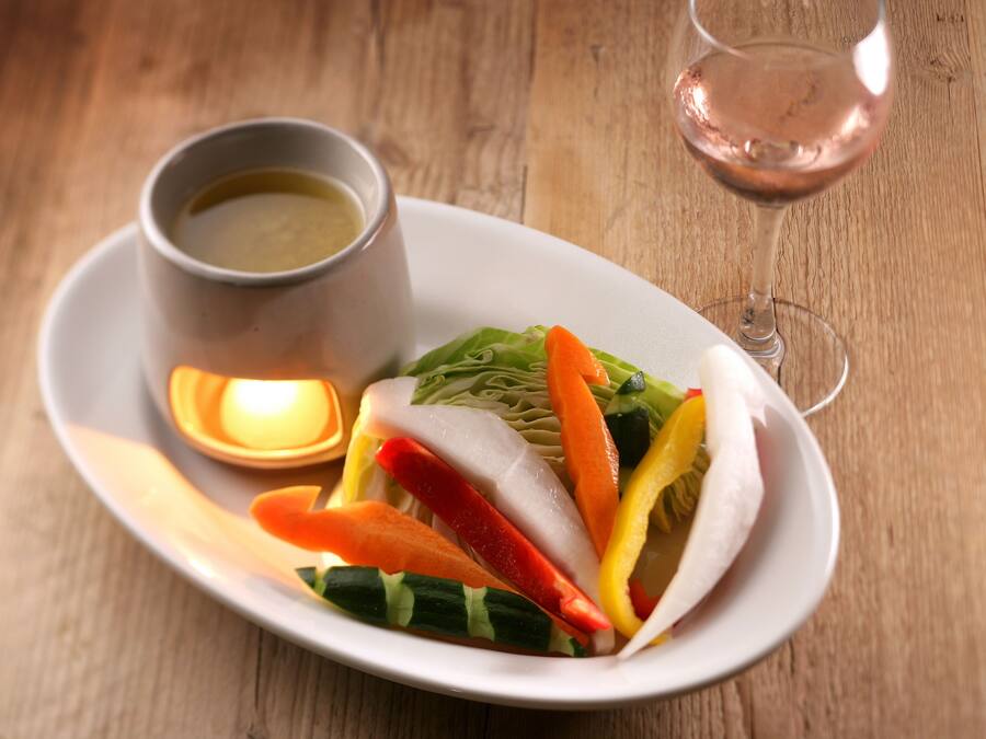 A plate of sliced vegetables and a glass of wine on a wooden table.