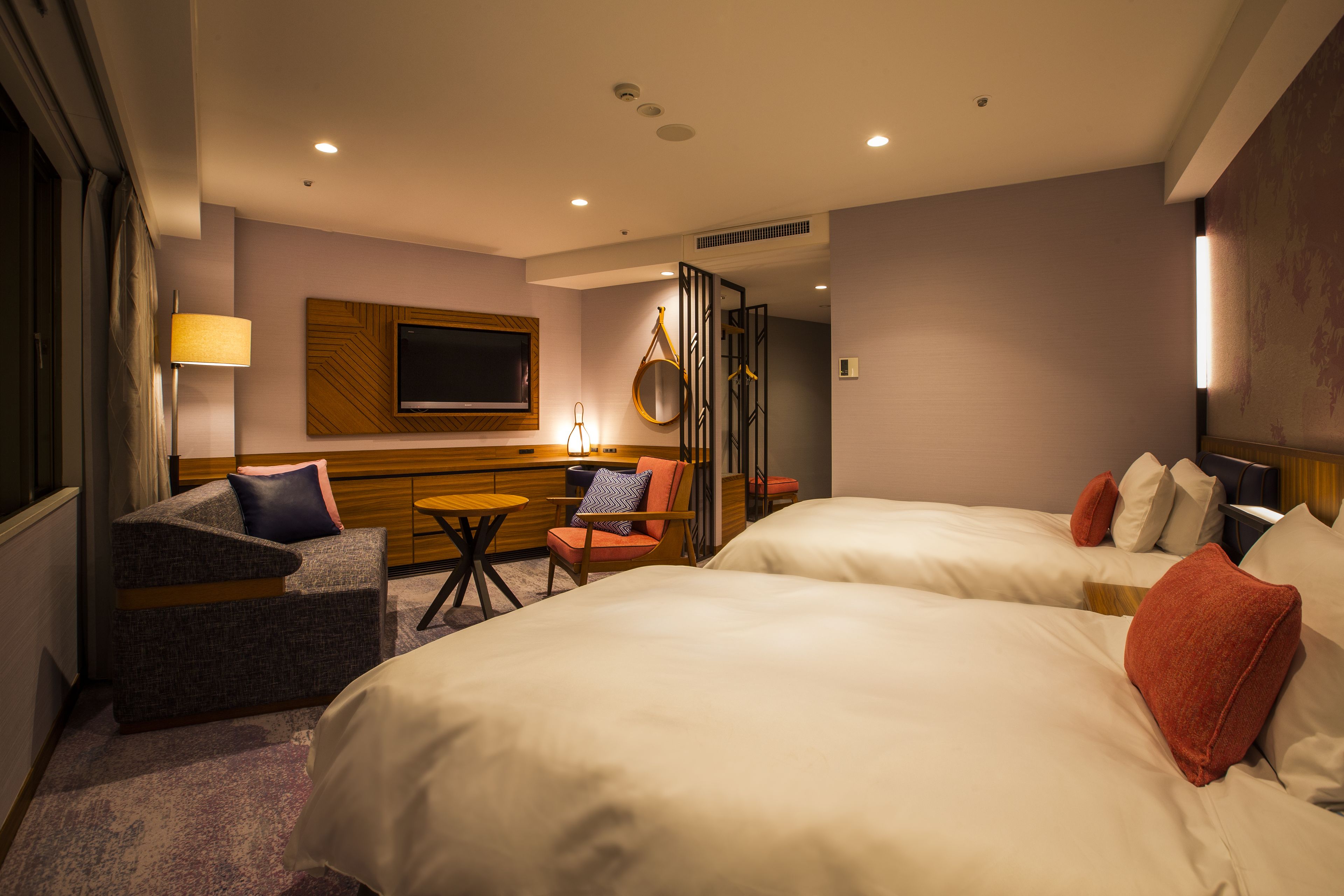 A hotel room with two beds, a sofa, a small table, and a TV mounted on the wall.