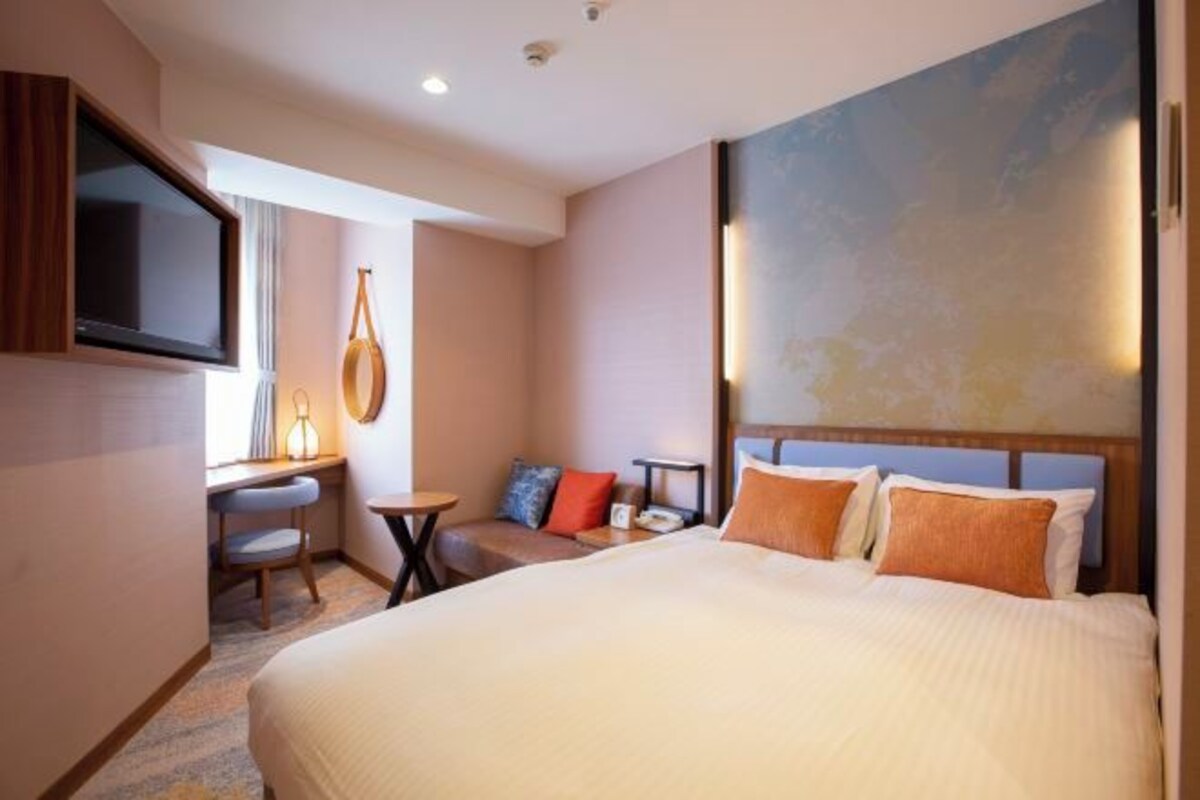 Une chambre d’hôtel avec un grand lit, un bureau avec une chaise, une petite table et un téléviseur fixé au mur.