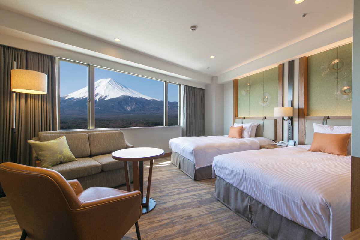A hotel room with two beds, a sofa, a small table, and a view of a mountain.