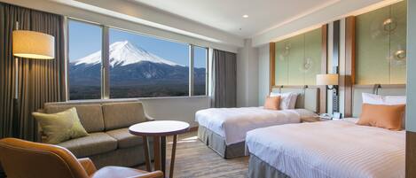 A hotel room with two beds, a sofa, a small table, and a view of a mountain.