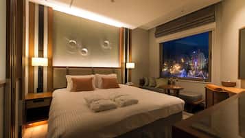 Habitación de hotel con una cama grande, televisión, ventana con vista a la ciudad y escritorio con lámpara.