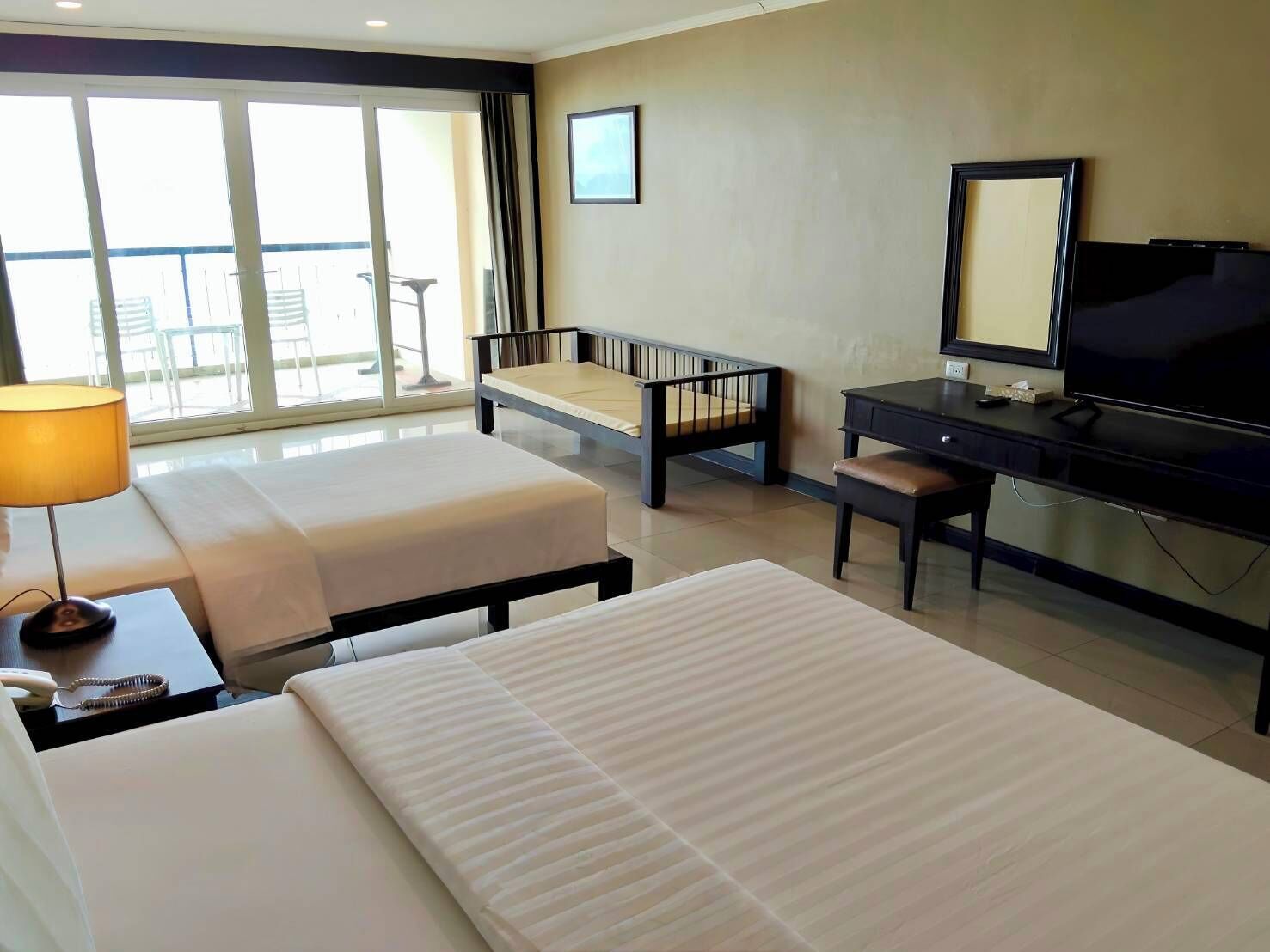 Una habitación de hotel con dos camas, un escritorio, televisor y un balcón con sillas.