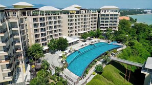 Un hotel de varios pisos con una amplia piscina curvo, mobiliario exterior y abundante vegetación.