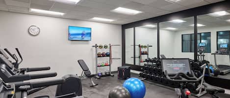 A gym with treadmills, exercise balls, dumbbells, and a TV screen displaying workout information.