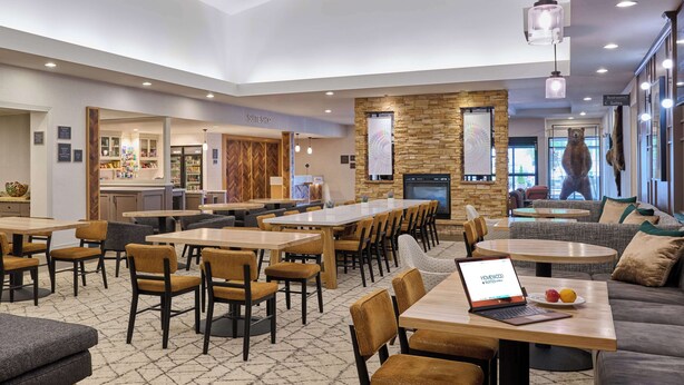 A modern hotel lobby with a dining area, sofas, and a fireplace. - Homewood Suites by Hilton Anchorage (Anchorage)