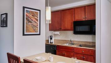 A compact kitchen with wooden cabinets, a microwave, and a dishwasher. There is a framed picture on the wall and a table set with plates and cups.