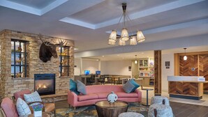 A hotel lobby with a stone fireplace, a pink sofa, and a 'Suite Shop' sign. - Homewood Suites by Hilton Anchorage (Anchorage)