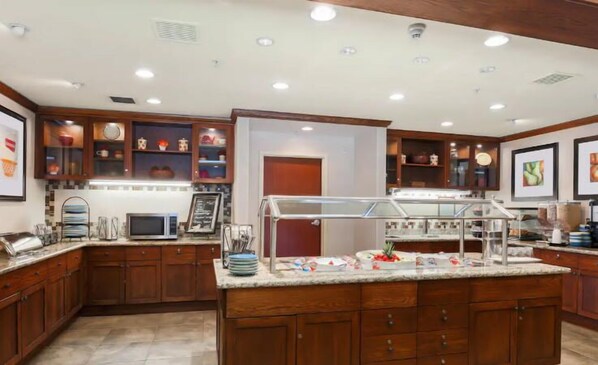 A well-lit kitchen with wooden cabinets, a marble countertop, and a glass display case. - Homewood Suites by Hilton Anchorage (Anchorage)