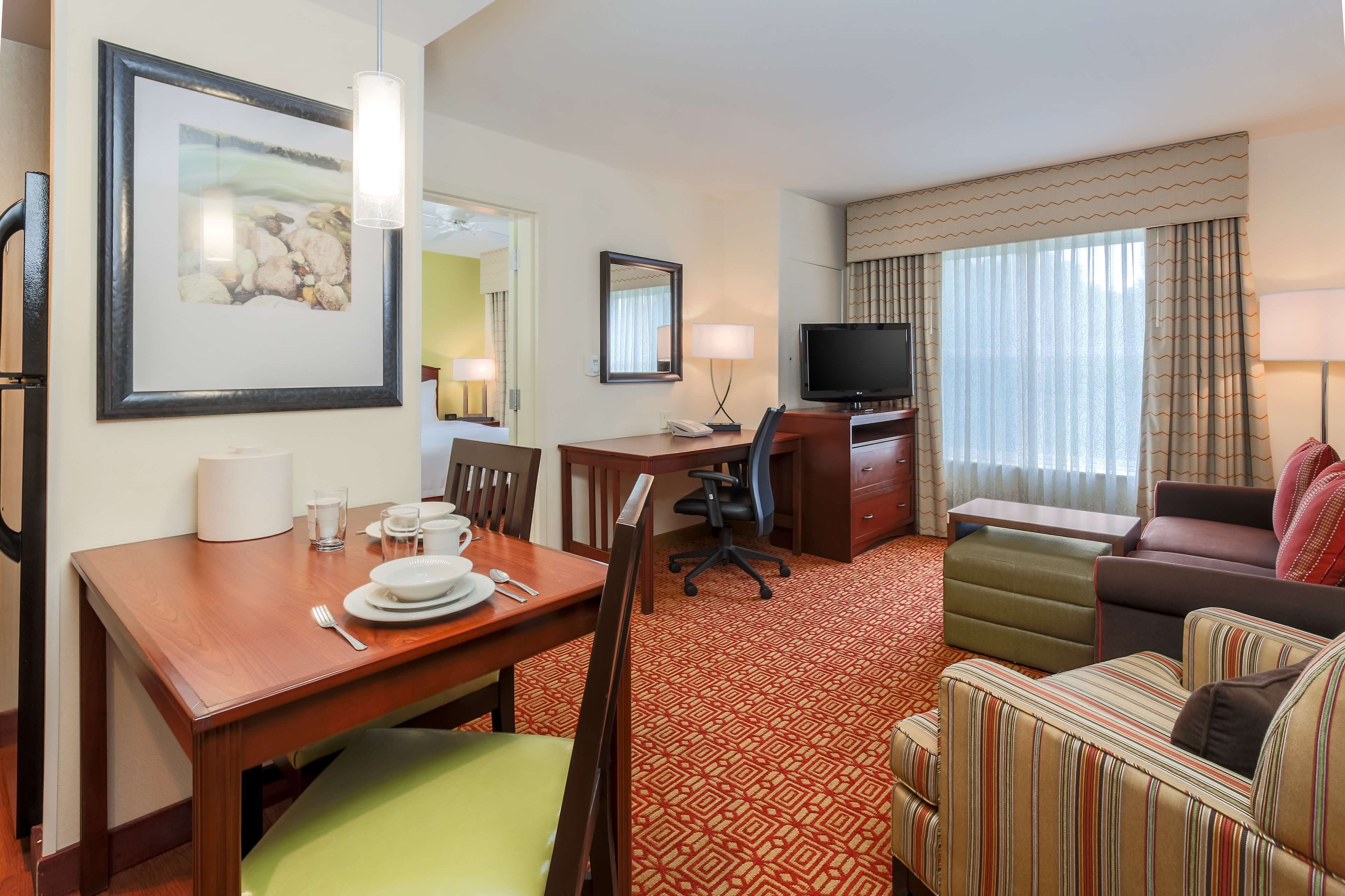A hotel room with a dining table set for two, a television, a sofa, and a patterned carpet.
