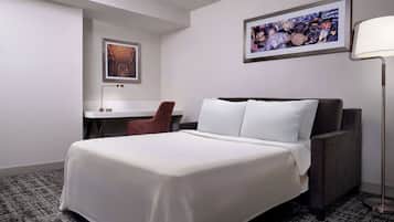 A hotel room with a large bed, a desk, a chair, and a lamp.