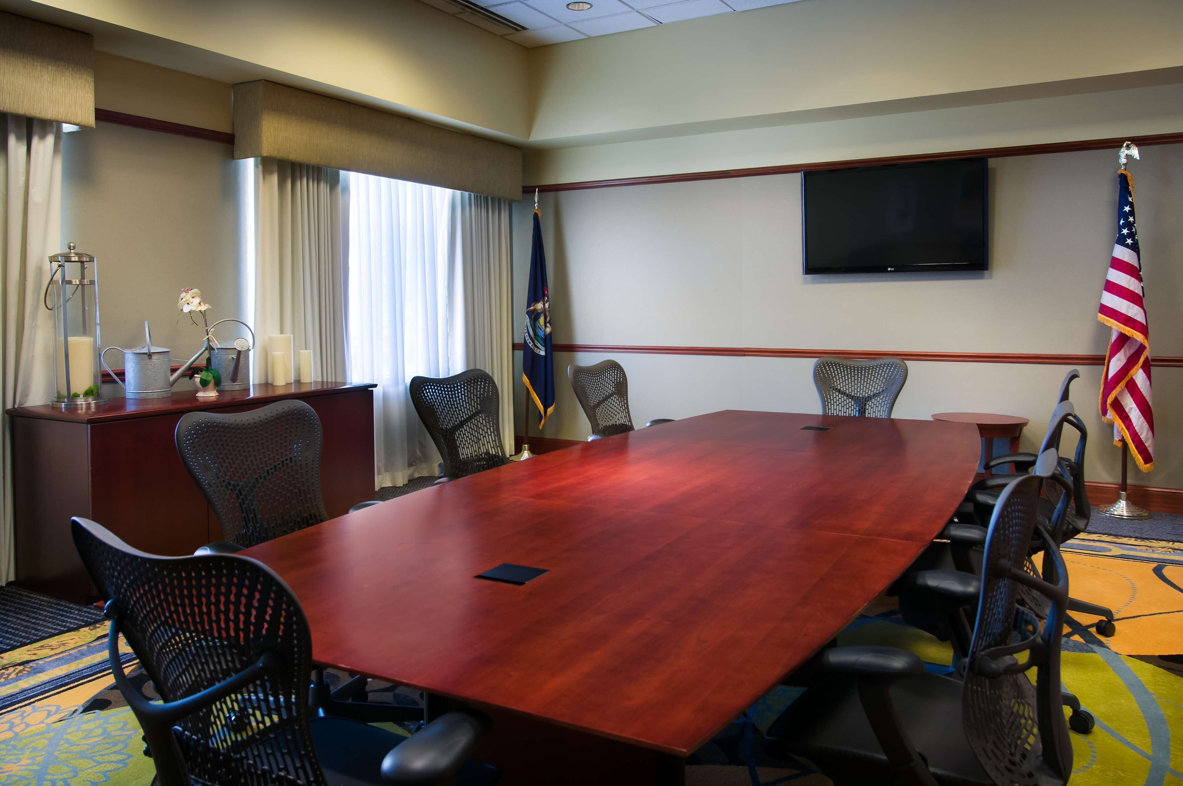 A conference room with a large wooden table, eight chairs, a flag, a television, and a flagpole.