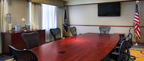 A conference room with a large wooden table, eight chairs, a flag, a television, and a flagpole.