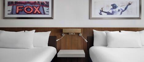 A hotel room with two beds, a wooden headboard, a small table, and two framed pictures on the wall.